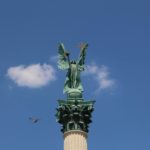 a bird flying near millennium monument under blue sky