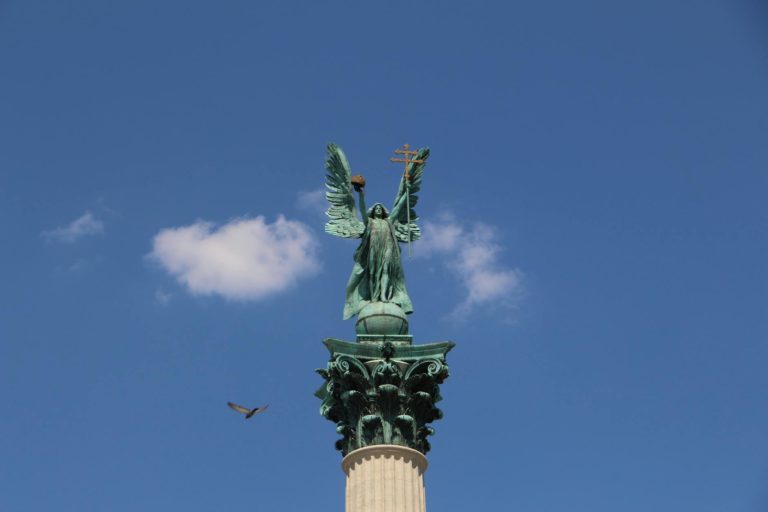 a bird flying near millennium monument under blue sky